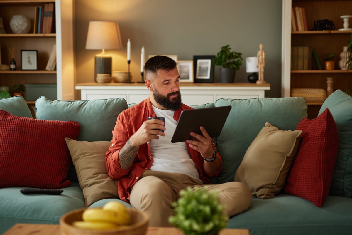 Tattooed man sitting on sofa using digital tablet at home