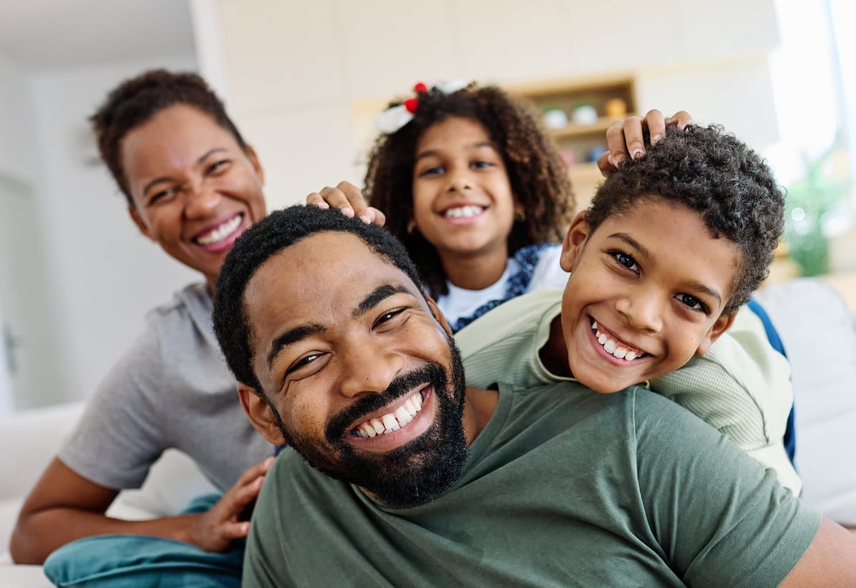 Portrait of a happy Black family of five - mother, father and children - together on the couch at home, symbolizing the full life faith, family, and connection bring